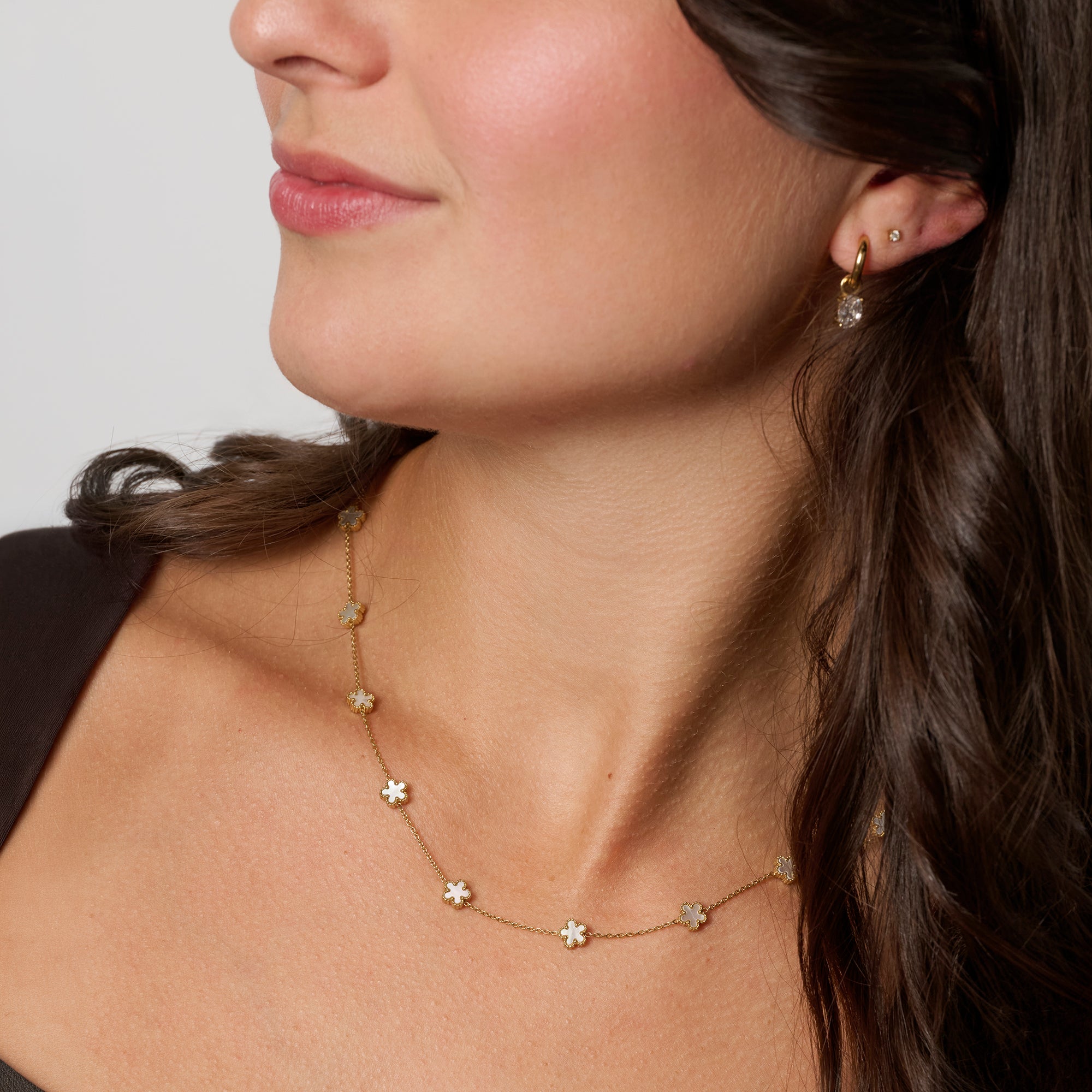 A close-up of a woman wearing a delicate gold necklace with small flower charms and gold earrings. Waterproof, stainless steel and allergy free. By MIAJWL.
Gros plan d'une femme portant un collier doré délicat orné de petites fleurs et des boucles d'oreilles dorées. Résistant à l'eau, en acier inoxydable et hypoallergénique. Par MIAJWL.