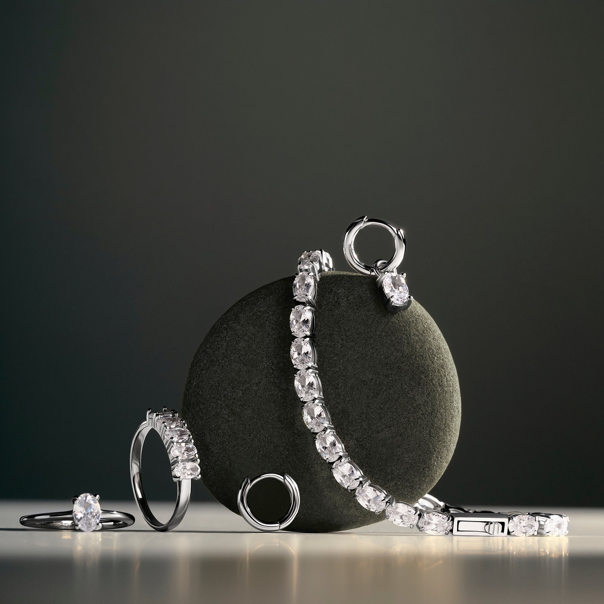 Silver rings, earrings and a tennis bracelet set with oval clear stones, displayed against a round dark stone on a dark background. Nickel-free, waterproof & tarnish-resistant stainless steel jewelry for sensitive skin.
Bagues, boucles d'oreilles anneaux et bracelet tennis argentés sertis de pierres transparentes ovales, présentés contre une pierre ronde foncée sur fond sombre. Bijoux en acier inoxydable sans nickel, résistants à l'eau et anti-ternissement pour peaux sensibles.