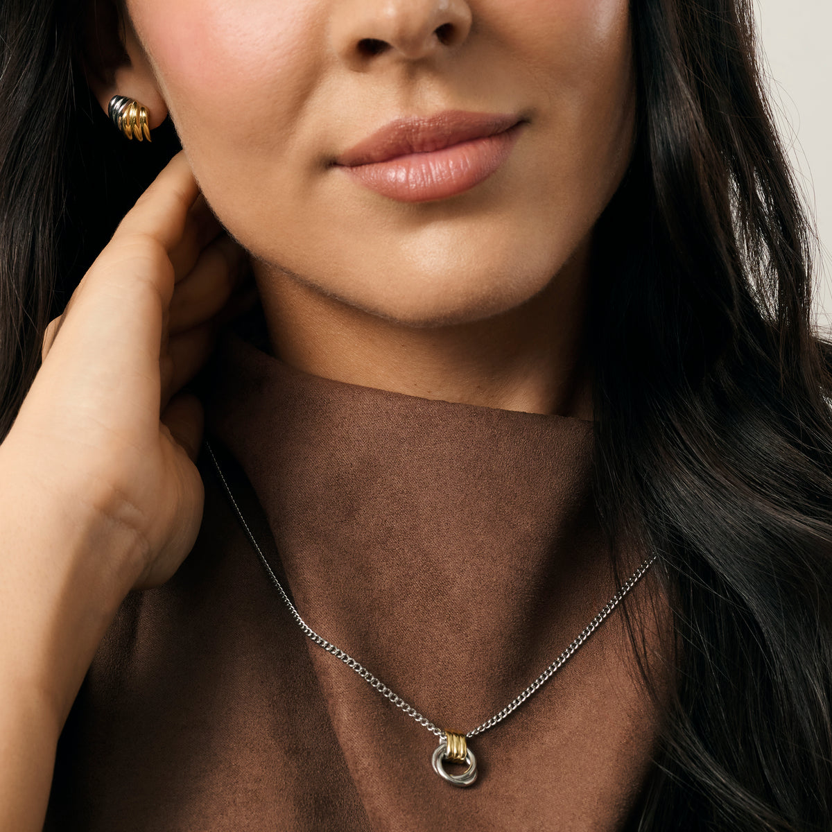 A close-up lifestyle shot of a model wearing a two-tone chain necklace and two-tone earrings paired with a brown top. Waterproof, stainless steel and allergy free. By MIAJWL.
Photo lifestyle en gros plan d'un mannequin portant un collier à chaîne deux tons et des boucles d'oreilles deux tons, agencés avec un haut brun. Résistant à l'eau, en acier inoxydable et hypoallergénique. Par MIAJWL.