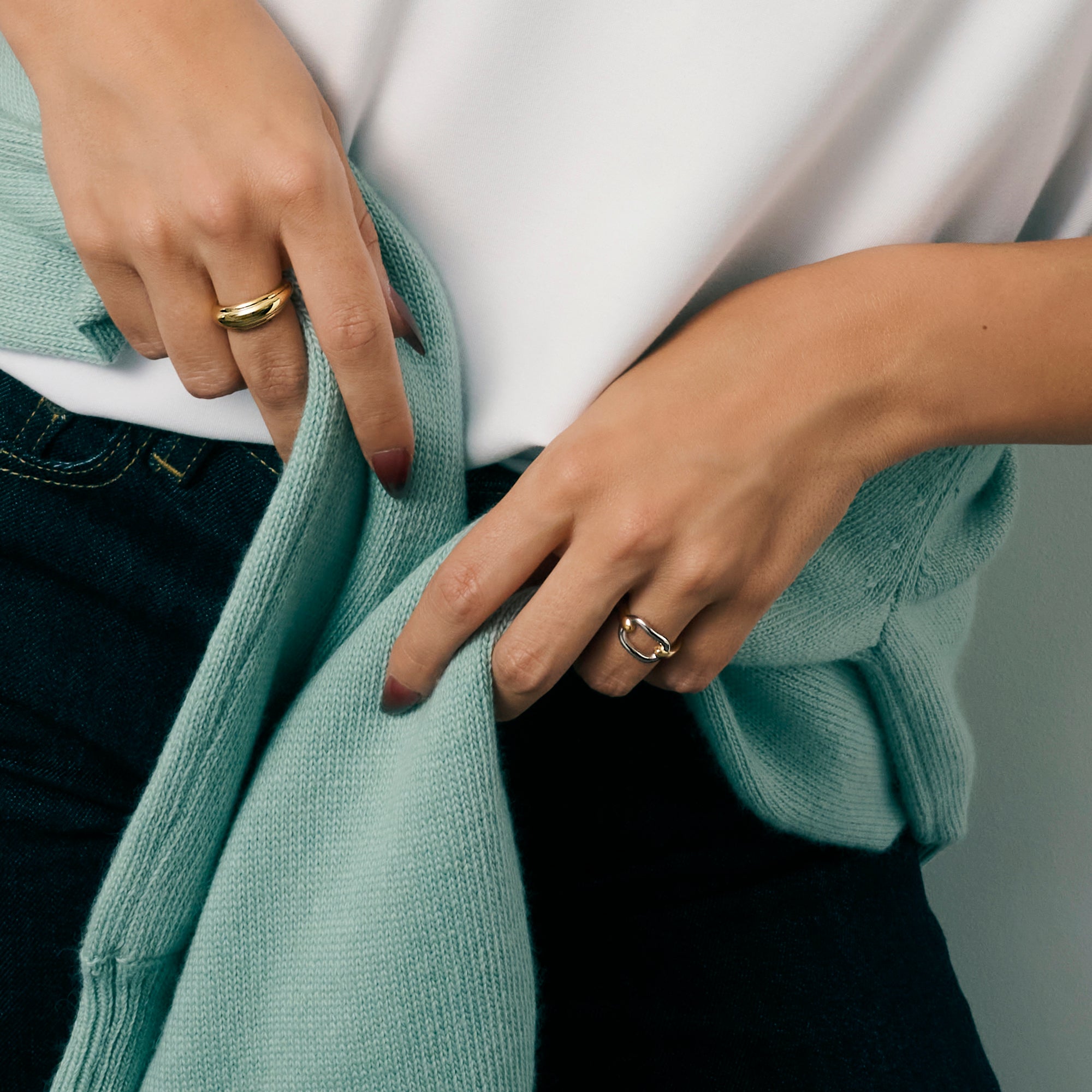 Close-up of a model's hands wearing a gold dome ring and a two-tone gold and silver ring, styled with a mint green cardigan, white top and dark jeans. Nickel-free, waterproof & tarnish-resistant.

Gros plan sur les mains d'un mannequin portant une bague dôme dorée et une bague à maillon bicolore dorée et argentée, agencées avec un cardigan vert menthe, un haut blanc et un jeans foncé. Bagues en acier inoxydable sans nickel, résistantes à l'eau et anti-ternissement.